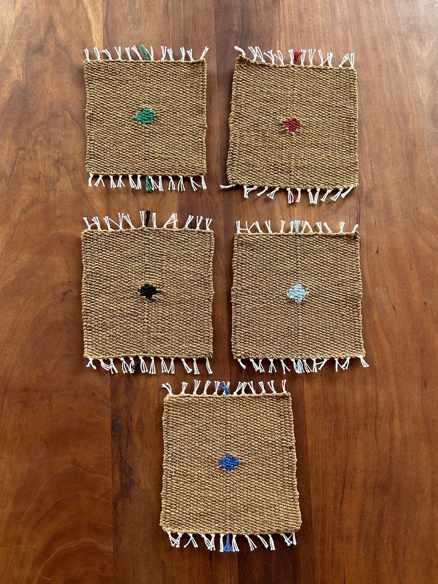 Set of woven coasters with colorful embellishments on a wooden surface