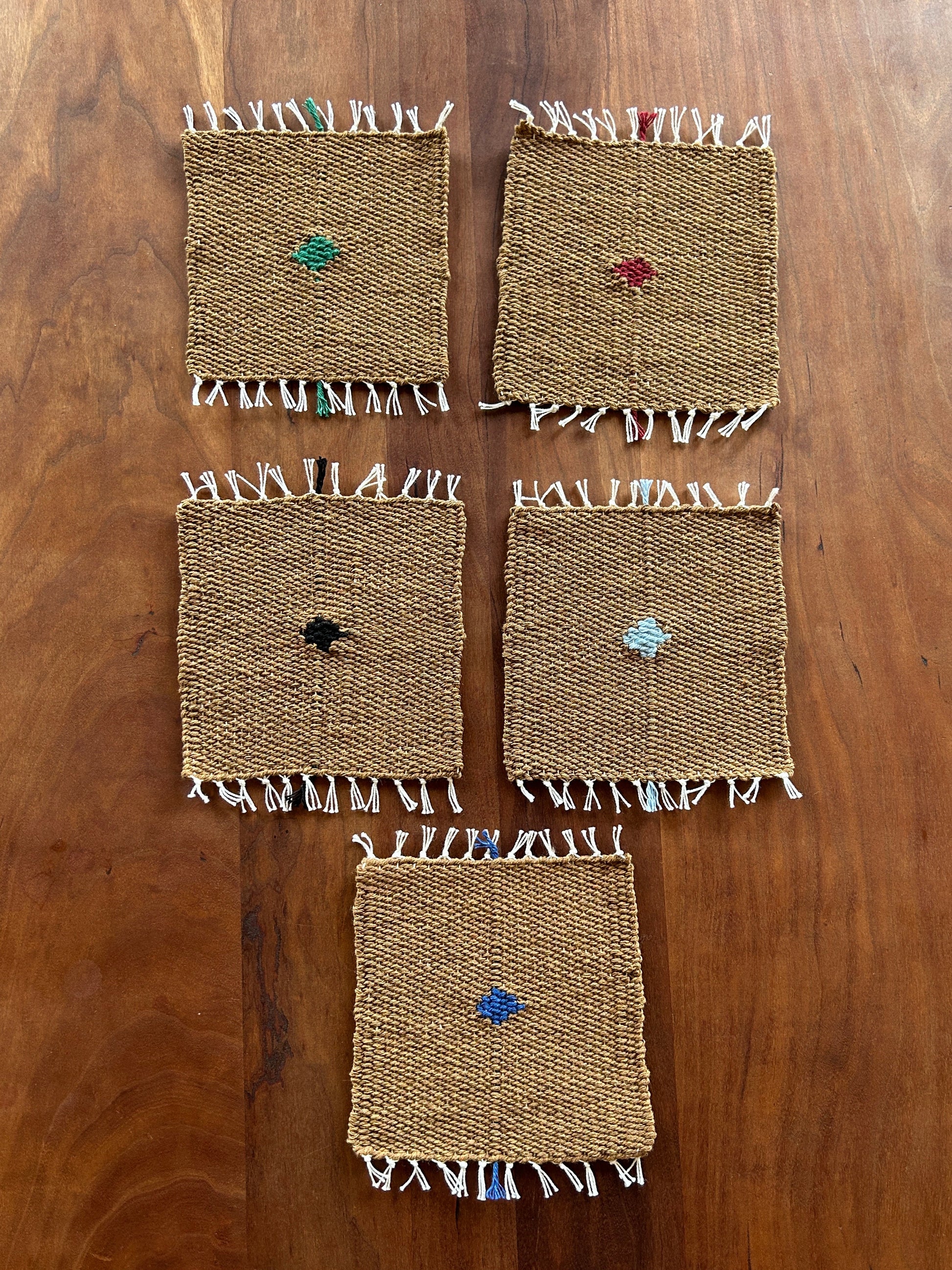 Set of woven coasters with colorful embellishments on a wooden surface