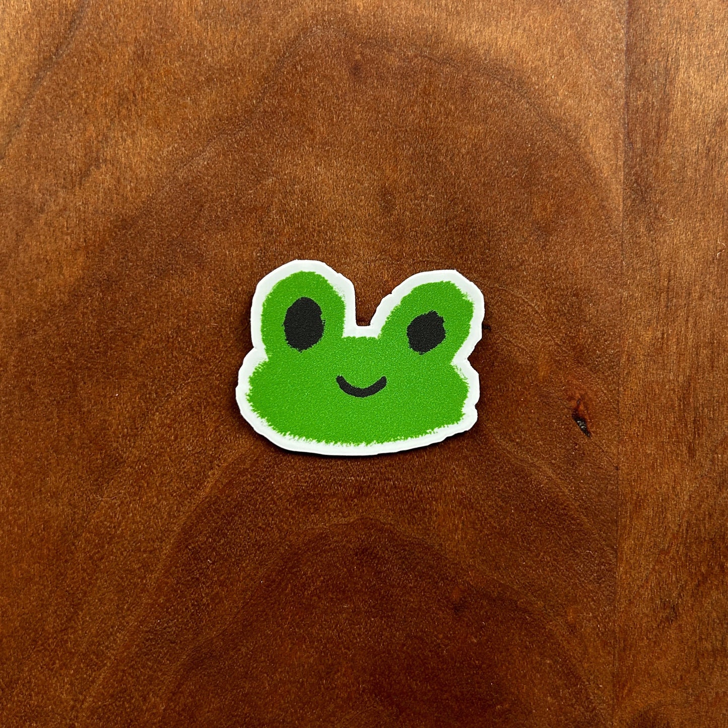 Green cartoon frog sticker on a wooden surface
