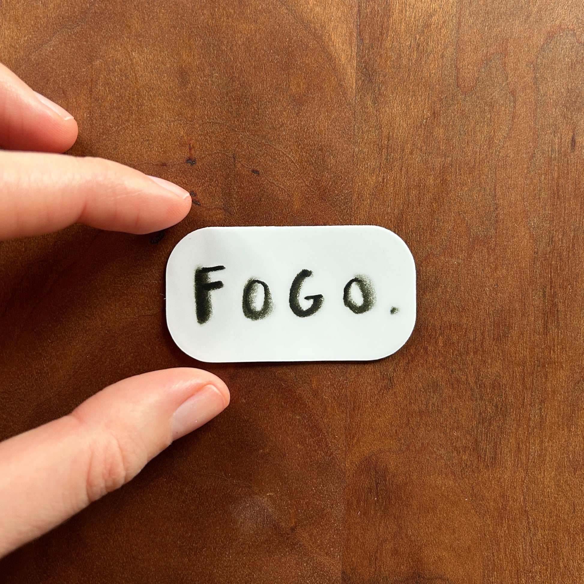 Hand holding a small white rectangular object with 'FOGO' on it against a wooden background